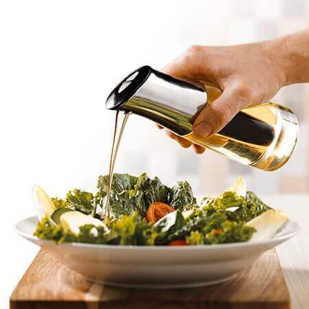 Salada fresca sendo temperada com azeite usando utensílios de cozinha gourmet em ambiente moderno