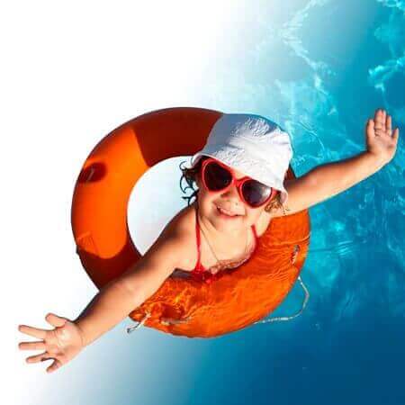 Criança sorridente na piscina usando acessórios para praia e piscina incluindo boia, óculos e chapéu branco